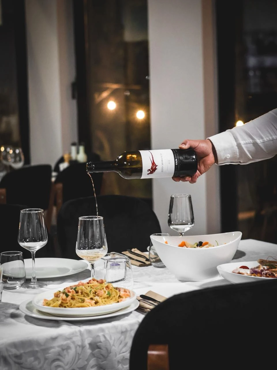 Verë duke u derdhur pranë pjatave me pasta dhe fruta deti në tarracën e Clandestino