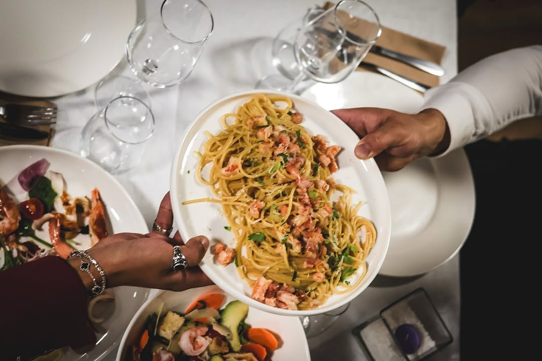 Pasta duke u shërbyer nga lart, tavolinë me gota verë dhe pjata